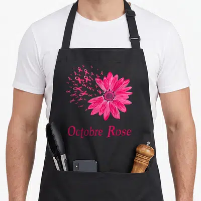 Tablier de cuisine noir avec une grande fleur rose et des rubans formant un nuage, texte Octobre Rose en bas.