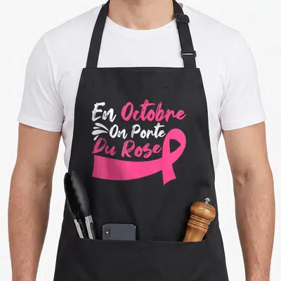 Tablier de cuisine noir avec l'inscription En Octobre On Porte Du Rose et un grand ruban rose vif imprimé au centre.