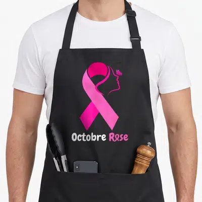 Tablier de cuisine noir avec grand ruban rose, profil féminin stylisé, papillon et texte Octobre Rose en bas.
