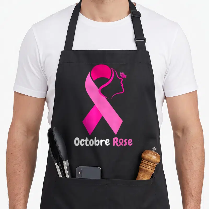Tablier de cuisine noir avec grand ruban rose, profil féminin stylisé, papillon et texte Octobre Rose en bas.