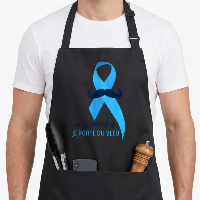 Tablier de cuisine noir avec ruban bleu, moustache noire et texte en novembre je porte du bleu imprimé au centre.