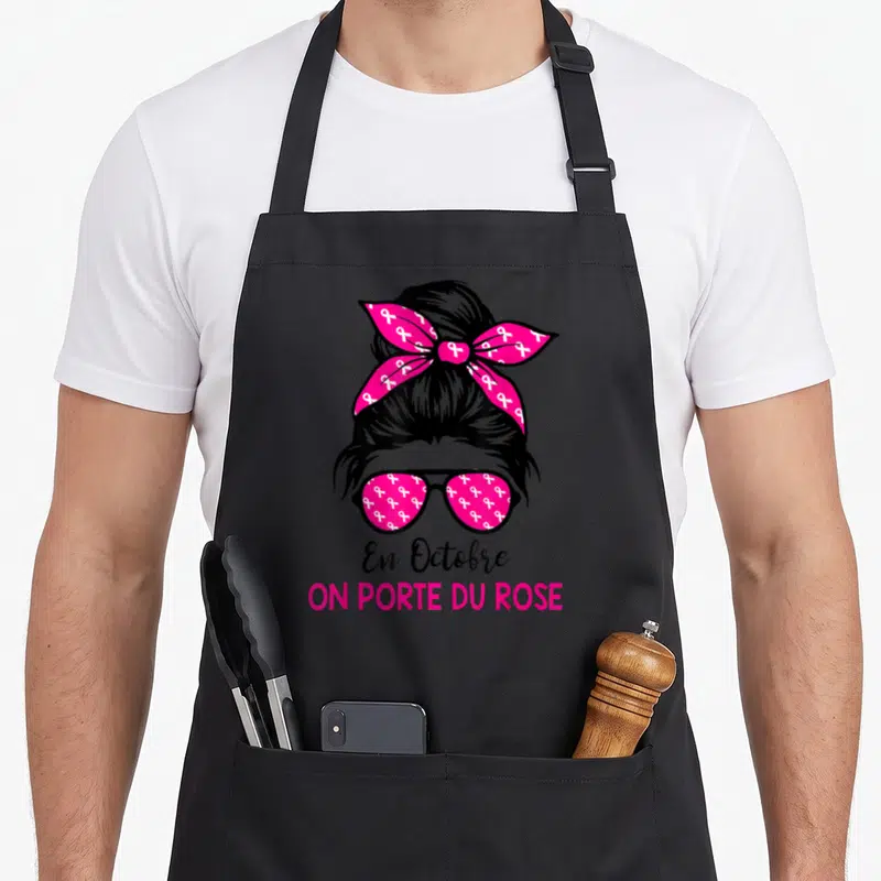 Tablier de cuisine noir avec illustration femme chignon rubans roses lunettes et texte En Octobre on porte du rose