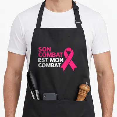 Tablier de cuisine noir avec inscription Son Combat Est Mon Combat et ruban rose symbolique.