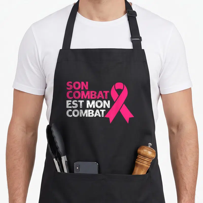 Tablier de cuisine noir avec inscription Son Combat Est Mon Combat et ruban rose symbolique.