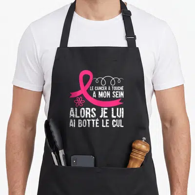 Tablier de cuisine noir avec ruban rose et texte blanc humoristique sur le cancer du sein.