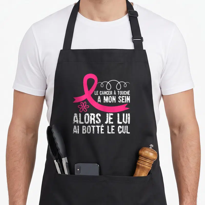 Tablier de cuisine noir avec ruban rose et texte blanc humoristique sur le cancer du sein.