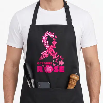 Tablier de cuisine noir avec un grand ruban rose composé de papillons, le texte OCTOBRE ROSE et une fleur en bas.