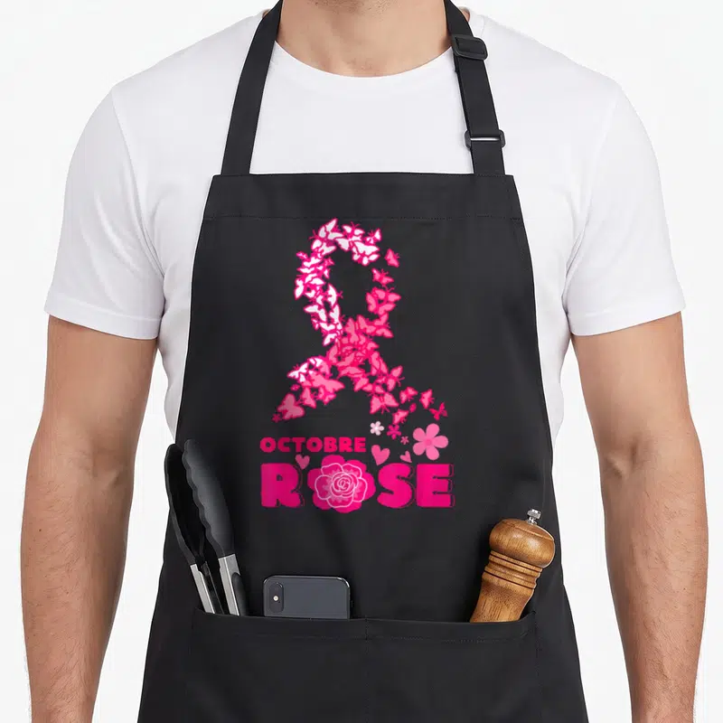 Tablier de cuisine noir avec un grand ruban rose composé de papillons, le texte OCTOBRE ROSE et une fleur en bas.