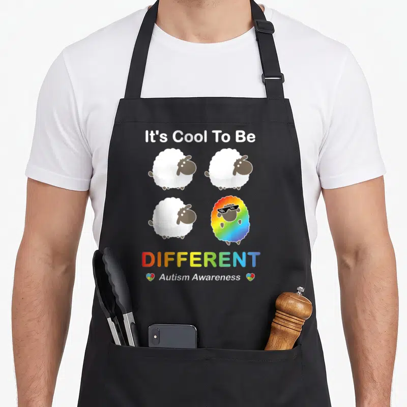 Tablier de cuisine noir avec trois moutons blancs et un mouton arc-en-ciel portant des lunettes de soleil pixelisées.
