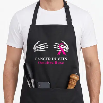 Tablier de cuisine noir avec deux mains squelettiques blanches tenant un ruban rose et le texte Cancer du Sein Octobre Rose.