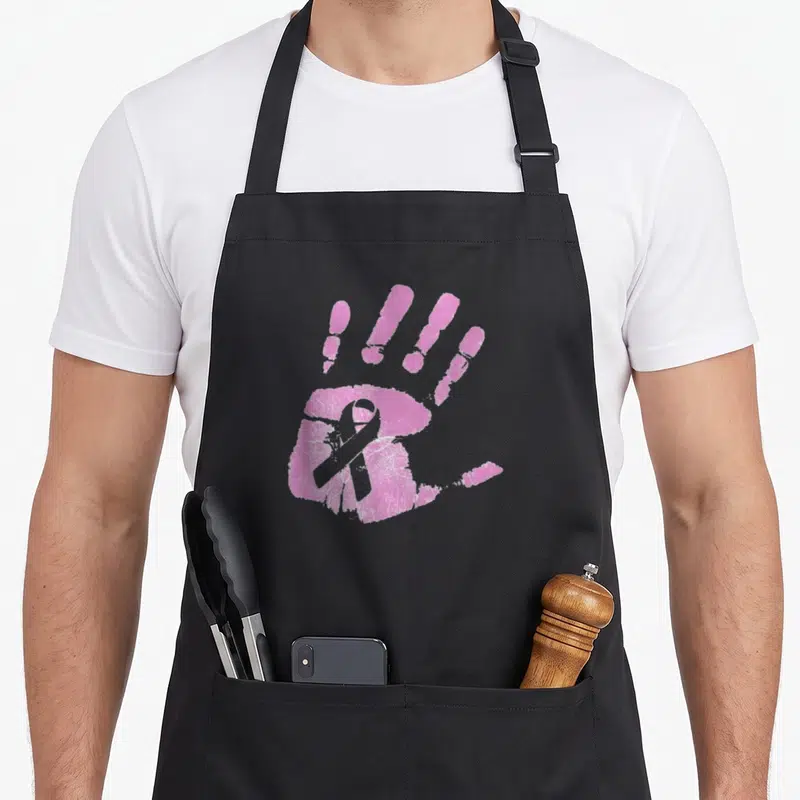 Tablier de cuisine noir avec une empreinte de main rose contenant un ruban de sensibilisation au cancer du sein.