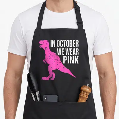 Tablier de cuisine noir avec silhouette dinosaure rose et texte blanc In October Nous Portons Pink