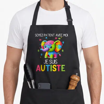 Tablier de cuisine noir avec un éléphant multicolore en puzzle et le texte Soyez Patient Avec Moi Je Suis Autiste.