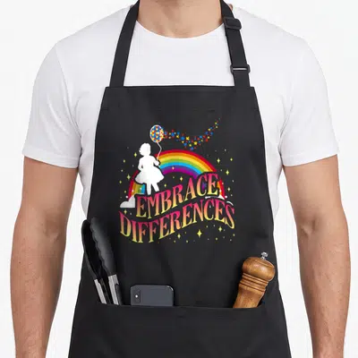 Tablier de cuisine noir avec une silhouette tenant un ballon arc-en-ciel et le texte Embrace Differences en lettres colorées.