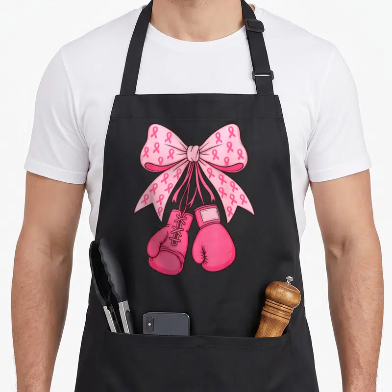 Tablier de cuisine noir avec grand nœud rose motif rubans et gants de boxe roses suspendus.