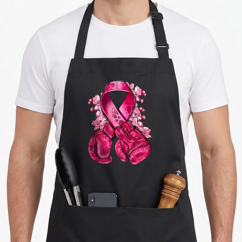 Tablier de cuisine noir avec ruban rose floral et gants de boxe roses croisés au centre.