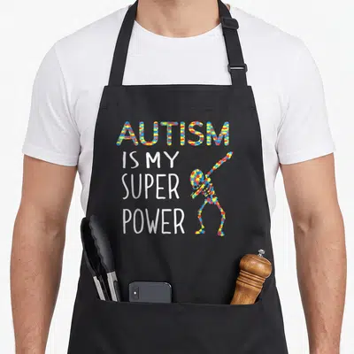 Tablier de cuisine noir avec inscription Autism is My Super Power et silhouette en pièces de puzzle multicolores.