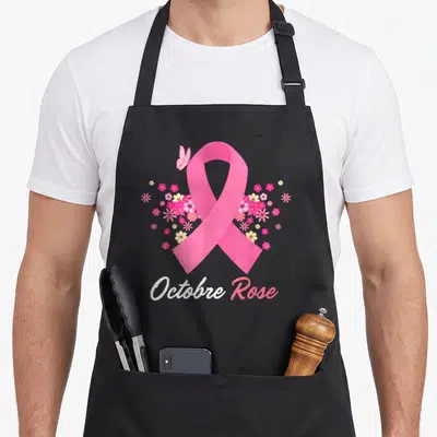 Tablier de cuisine noir avec un grand ruban rose entouré de fleurs colorées et d'un petit papillon en haut à gauche.