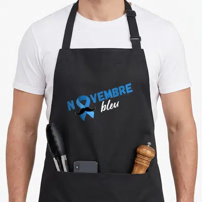 Tablier de cuisine noir avec un ruban bleu formant le O de novembre et une moustache noire stylisée.
