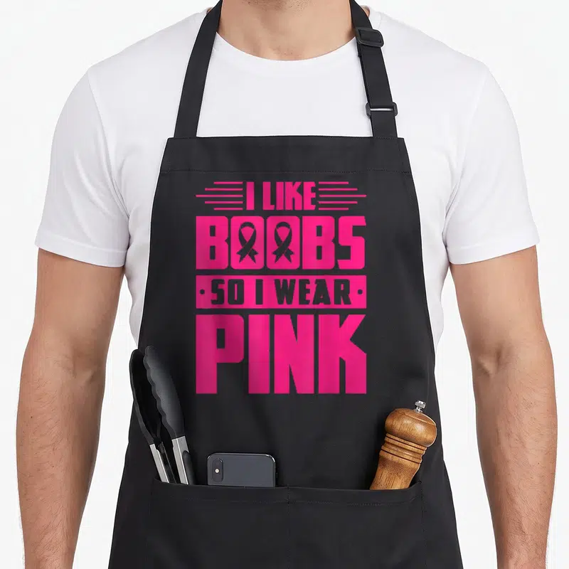 Tablier de cuisine noir avec l'inscription « I Like Boobs So I Wear Pink » en rose vif et gris.