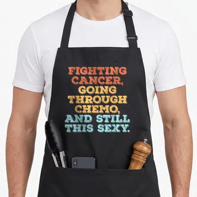 Tablier de cuisine noir avec un texte coloré en anglais sur fond uni gris clair.