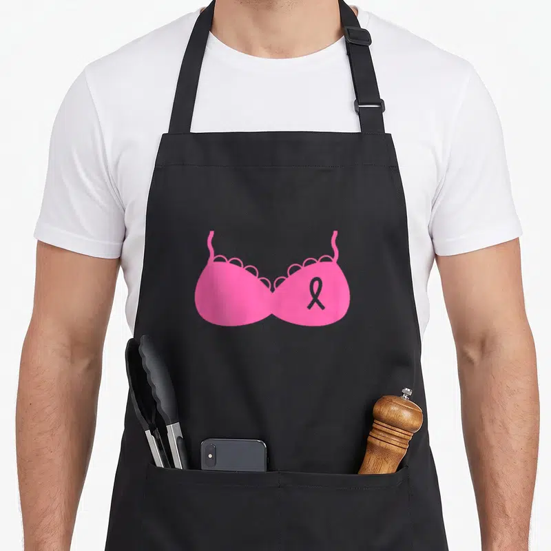 Tablier de cuisine noir avec illustration soutien Octobre Ruban Rose Combattre Cancer Du Sein sur fond uni gris.