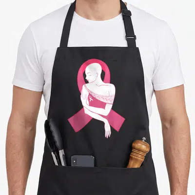 Tablier de cuisine noir avec illustration d'une femme tondue dans un grand ruban rose symbolisant la lutte contre le cancer du sein.