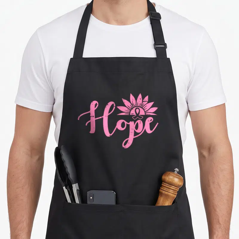 Tablier de cuisine noir avec l'inscription Hope en rose et un ruban stylisé en fleur.