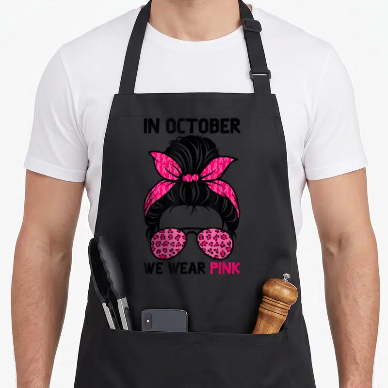 Tablier de cuisine noir avec un chignon rose orné de rubans et des lunettes à motifs léopard rose.