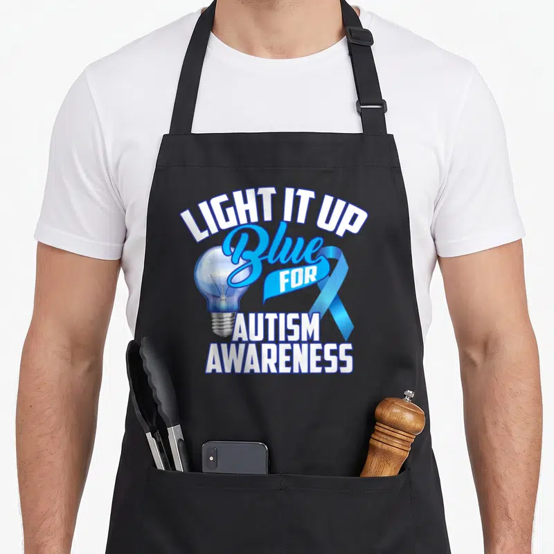Tablier de cuisine noir avec une ampoule bleue, un ruban et le texte Light It Up Blue for Autism Awareness.