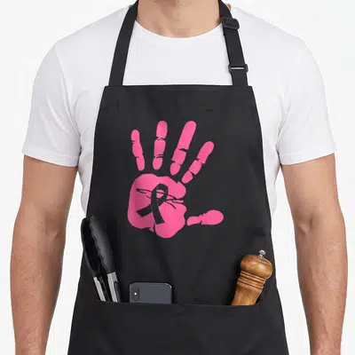 Tablier de cuisine noir avec une grande empreinte de main rose contenant un ruban gris symbolisant la lutte contre le cancer du sein.