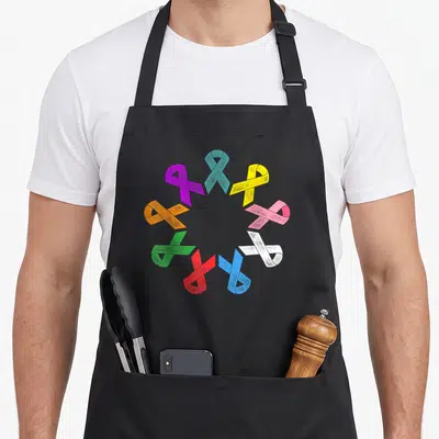 Tablier de cuisine noir avec un cercle de rubans multicolores à texture esquissée représentant divers cancers.