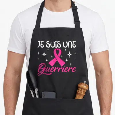 Tablier de cuisine noir avec un ruban rose et l'inscription Je suis une Guerriere entourée d'étoiles blanches.