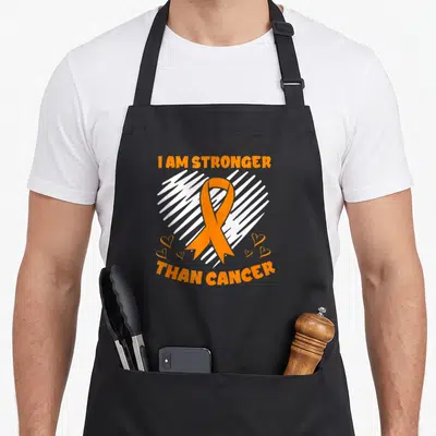 Tablier de cuisine noir avec un ruban orange et le texte I am stronger than cancer sur fond blanc esquissé.