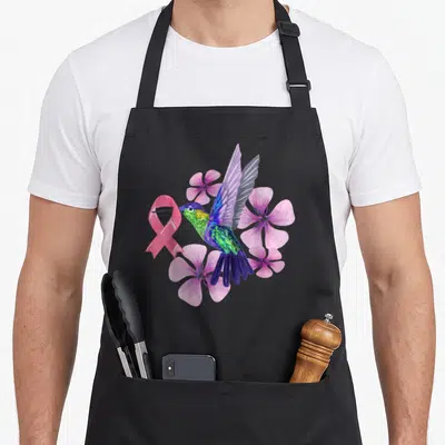 Tablier de cuisine noir avec un colibri multicolore tenant un ruban rose entouré de fleurs violettes.
