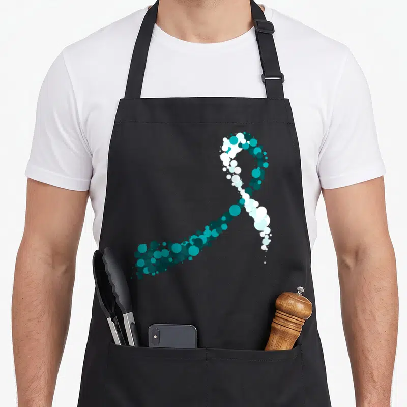 Tablier de cuisine noir avec un ruban bleu sarcelle stylisé composé de multiples cercles de tailles variées.