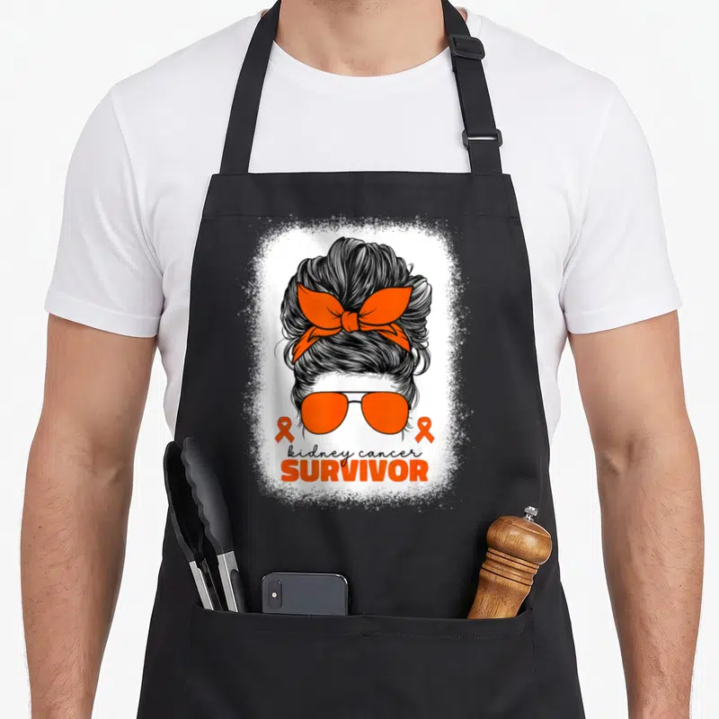 Tablier de cuisine noir avec illustration femme chignon ruban orange et texte kidney cancer survivor.