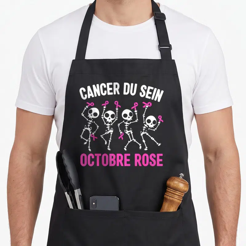 Tablier de cuisine noir avec quatre squelettes dansant tenant des rubans roses et le texte Cancer du Sein Octobre Rose.
