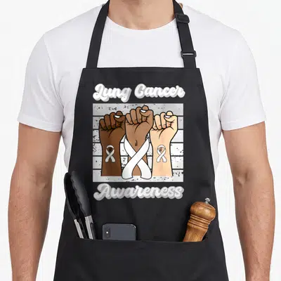 Tablier de cuisine noir avec trois poings levés de couleurs différentes et un ruban blanc croisé au centre.
