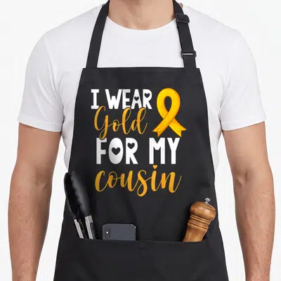 Tablier de cuisine noir avec un ruban doré et le texte Je porte de l'or pour mon cousin en blanc et jaune.