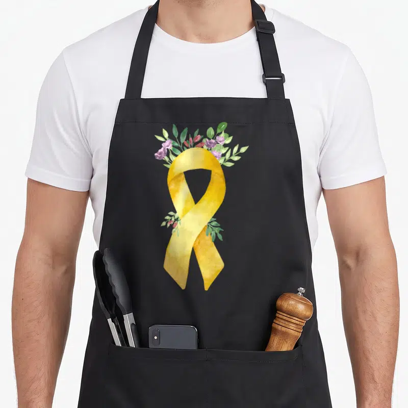 Tablier de cuisine noir avec un ruban doré aquarellé et une couronne de fleurs violettes et de feuilles vertes.