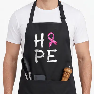 Tablier de cuisine noir avec inscription HOPE et ruban rose composé de petits cœurs roses et blancs.