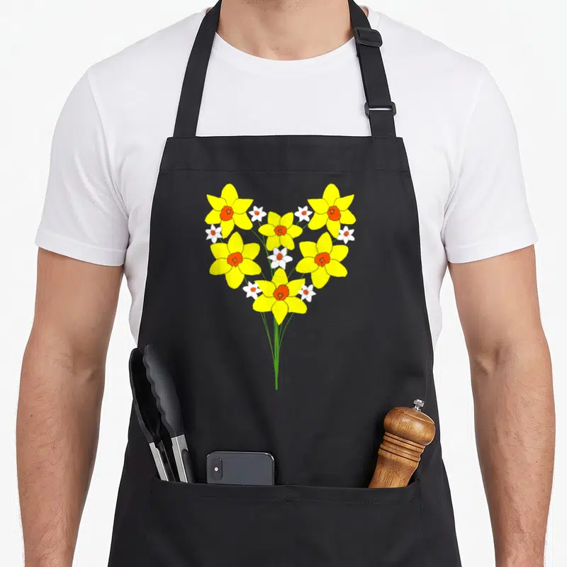 Tablier de cuisine noir avec bouquet de jonquilles jaunes et blanches formant un cœur sur fond uni.