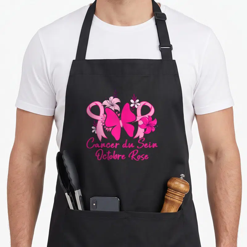 Tablier de cuisine noir avec un grand ruban rose, des fleurs colorées et le texte Cancer du Sein Octobre Rose en bas.