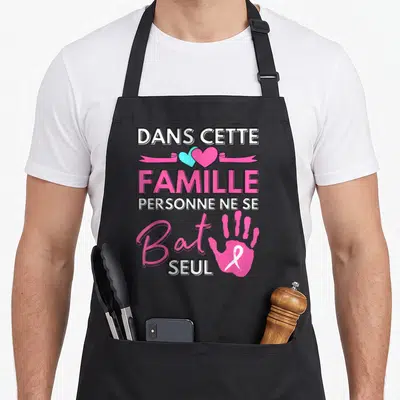 Tablier de cuisine noir avec inscription familiale, cœurs bicolores et main rose portant un ruban blanc.