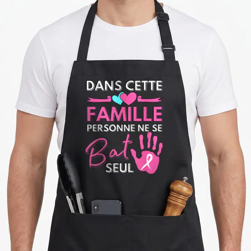 Tablier de cuisine noir avec inscription familiale, cœurs bicolores et main rose portant un ruban blanc.