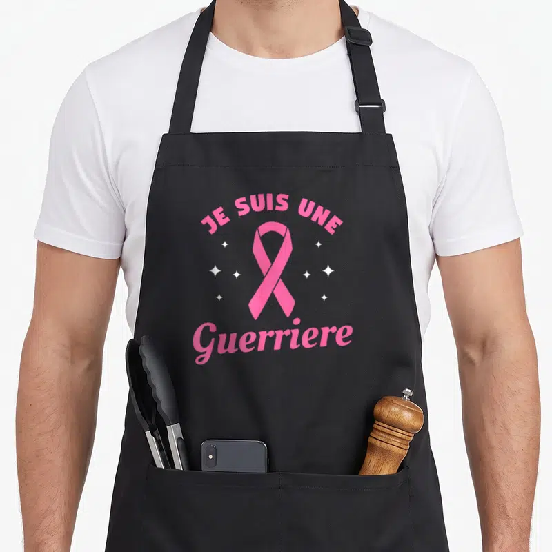 Tablier de cuisine noir avec un ruban rose, des étoiles blanches et le texte Je suis une Guerriere en lettres roses.