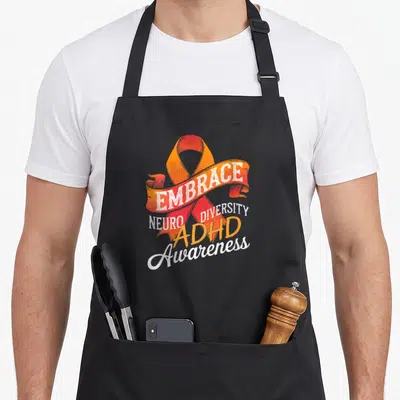 Tablier de cuisine noir avec un ruban orange et les mots EMBRACE NEURO DIVERSITY ADHD Awareness imprimés en blanc et orange.