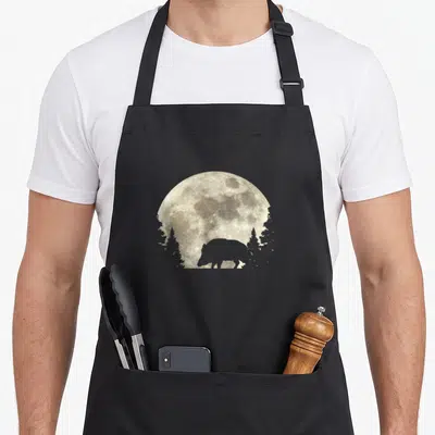 Tablier de cuisine noir avec silhouette de sanglier devant une lune détaillée et des arbres.