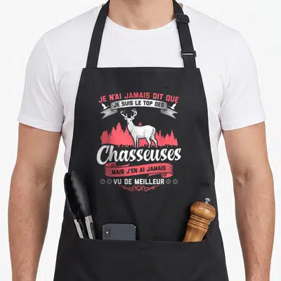 Tablier de cuisine noir avec illustration d'un cerf élaphe blanc sur fond de forêt rouge et texte humoristique en blanc et rose.